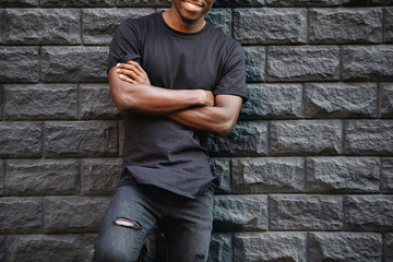 Man in blank black t-shirt standing against brick wall, cropped