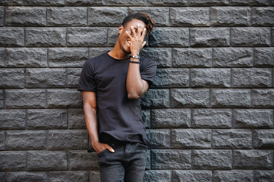 African american man in black t-shirt laughing against brick wall, palm on face