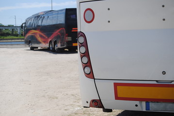 Dois autocarros um preto e um branco parados num parque de estacionamento á espera de seguirem viagem - turismo