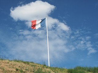 Nationalflagge von Frankreich vor blauem Himmel mit weißen Wolken auf grünem Hügel
