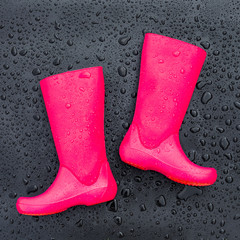 Trendy bright pink rubber boots on black wet surface covered with raindrops. Top view, space for text.