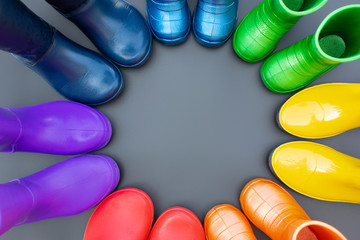 Colorful rubber boots of all colors of the rainbow-red, orange, yellow, green, blue, cyan and purple stand on the gray surface in a circle. Top view, space for text.