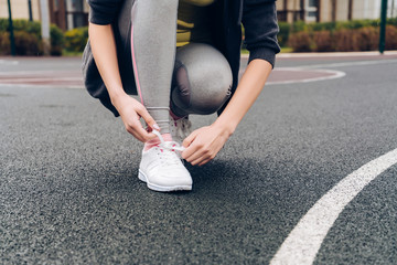 a slender girl in gray trousers tie shoelaces on her sneakers, on a sports ground, preparing for training
