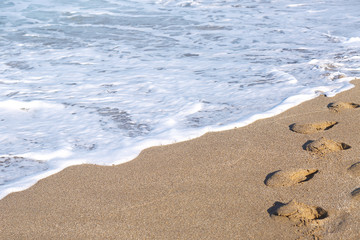 Fototapeta na wymiar Sea foam floods footprints on the beach