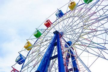 Large and bright ferris wheel against a clear blue sky. Long spokes and multi-colored seats. Concept of joy and good mood