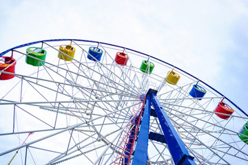 Large and bright ferris wheel against a clear blue sky. Long spokes and multi-colored seats. Concept of joy and good mood