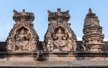 Shravanabelagola, Karnataka, India - November 1, 2013: Brown stone with black mold statues in niches on edge of roof at Jain Tirth building shows also small scene of love making.