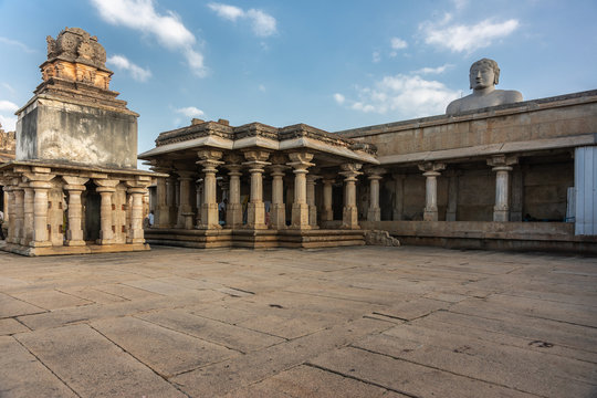 Shravanabelagola, Karnataka, India - November 1, 2013: Courtyard with tempe structures on pillars. Head of giant Bhagwan Bahubali peeps over them under blue sky with white clouds.