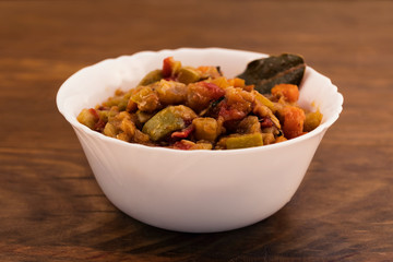Stewed vegetables-zucchini, tomatoes, pepper, carrots, onions in a white plate with bay leaf on a wooden background.