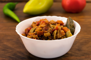 Cold appetizer of stewed in oil finely chopped vegetables, zucchini caviar with tomatoes, carrots and sweet pepper, in the background on the wooden surface of the whole vegetables.