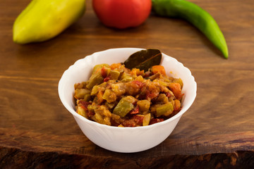 A cold vegetable appetizer of fried zucchini with tomatoes and carrots, laid out in a white porcelain plate against the background of whole fruits on a wooden surface.