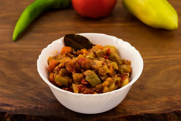 Appetizer of finely chopped vegetables, stewed in oil along with carrots, sweet pepper, tomatoes in white porcelain plate on wooden background.