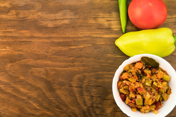 Light diet snack of fried oil zucchini with carrots, tomatoes and onions, laid out in a white porcelain plate on the background of whole fruits on a wooden surface, top view.