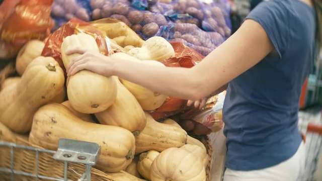 A woman in a supermarket buying vegetables, pumpkin