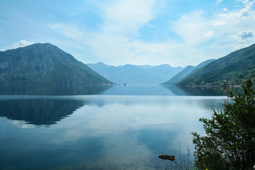 Fototapeta na wymiar Bay of Kotor, also known as Kotorska Boka, during a quiet summer afternoon with mountains reflecting in the waters of the Adriatic sea. The gulf of Kotor is one of most iconic landmarks of Montenegro.