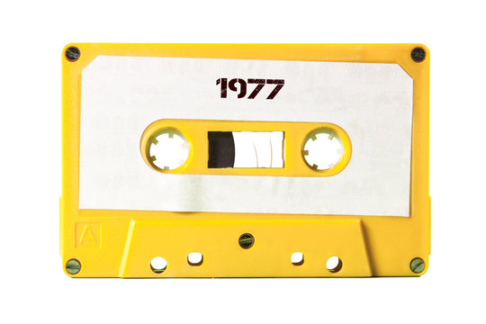A vintage cassette tape from the 1980s era (obsolete music technology) with the text 1977 printed over it (my addition, not in the original image). Color: white label, yellow plastic.
