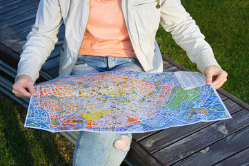 A tourist girl sits on a bench and looks at the map of Paris.