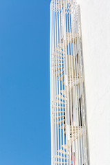 Spiral white staircase on the side of building against blue sky.