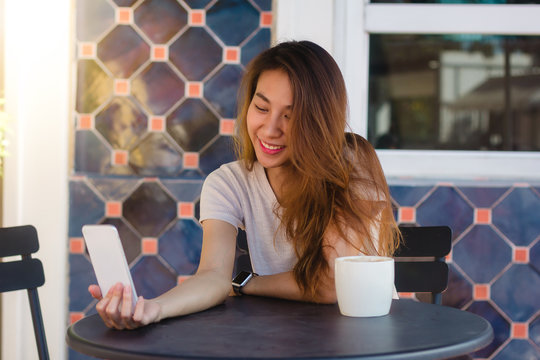 Attractive beautiful happy young Asian woman taking a selfie using a smart phone at cafe. Young Asian girl at restaurant taking self portrait.
