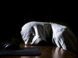 abstract anonymous person in the hood sleeping lying on the table in front of computer in the night