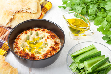 Bowl of delicious homemade hummus with cucumber sticks close-up