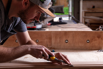 Close up of young  man builder wearing in a plaid shirt   treating a wooden product with a chisel in the workshop, close-up