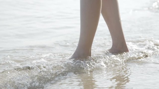 Female legs barefoot walks at the sea on the splashing waves. 4K