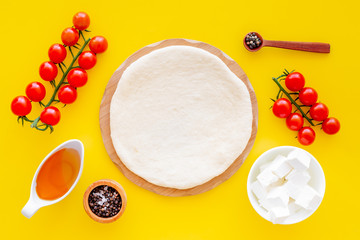 Ingredients for cooking vegetarian pizza. Rolled pizza dough, cherry tomatoes, olive oil, cheese mozzarella, spices on yellow background top view mockup