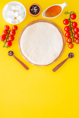 Obraz na płótnie Canvas Ingredients for cooking vegetarian pizza. Rolled pizza dough, cherry tomatoes, olive oil, cheese mozzarella, spices on yellow background top view mockup copy space