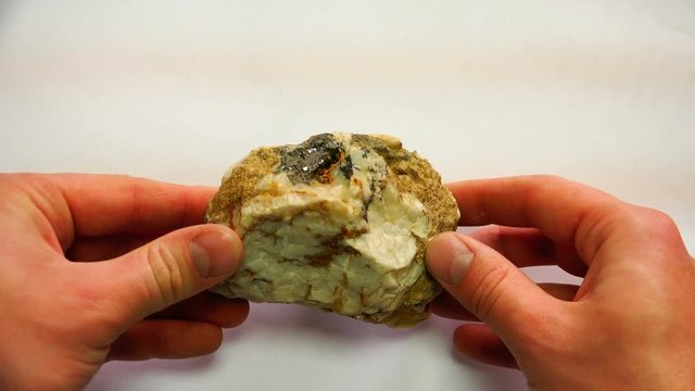 a mineral stone with veins twists in the hands of a specialist.