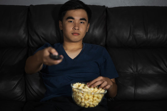 man holding remote control and watching TV while sitting on sofa at night