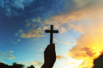 silhouette human hands praying to the GOD while holding a crucifix symbol with bright sunbeam on the sky