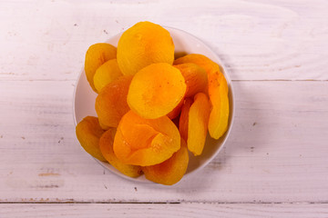 Ceramic plate with dried apricots on wooden table. Top view