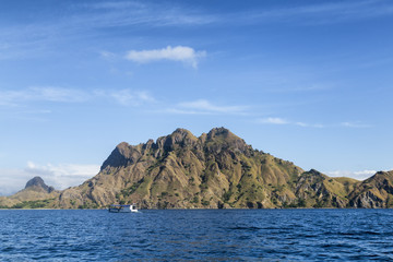 Fototapeta na wymiar A lone boat next to a cool looking mountain on Pulau Padar island in the Komodo National Park.