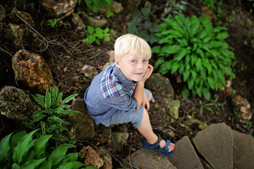 Naklejka na ściany i meble Peaceful Young Boy Sitting in Rock Garden by Green Hosta PLants on Summer Day