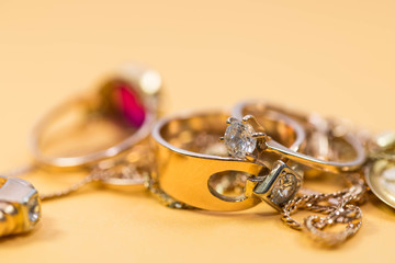 Real gold rings with diamond, chain, close up macro shot on yellow background.