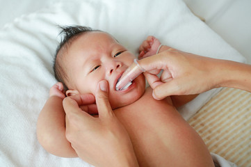 Close-up mother hand clean baby tongue and gum with soft rubber brush.