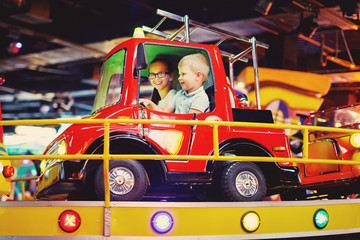 Cute teen girl and little boy ride on a carousel in a toy car arcade in game machine at an amusement park. © olgasparrow