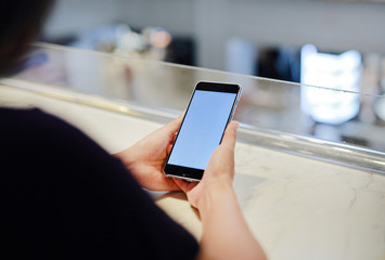 woman holding and using smartphone with blank white screen in cafe.