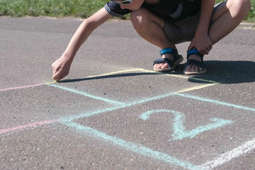 Boy is drawing hopscotch on the asphalt.