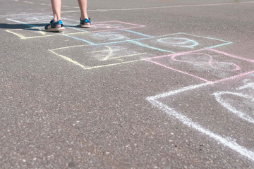 Boy jumps playing hopscotch in the street. Close-up legs.