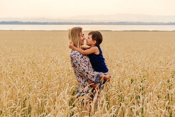 young happy beautiful mother with baby faces in wheat field