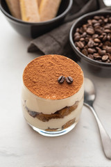 Traditional Italian dessert tiramisu in a glass on a white stone background. Copy space.