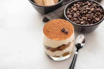 Traditional Italian dessert tiramisu in a glass on a white stone background. Copy space.