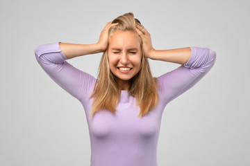 Mad crazy young woman in blue t shirt with hands on head and eyes closed standing and suffering from headache isolated over white background