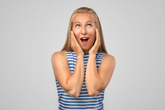 Horizontal shot of amazed shocked female notices something upwards, cant believe eyes, says wow and expresses surprisment, isolated over gray background. Beautiful excited blonde woman in studio