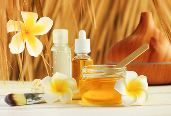 Honey spa with tropical flower frangipani decor, jars with golden beauty treatment oils for relaxing skin care under straw thatch.