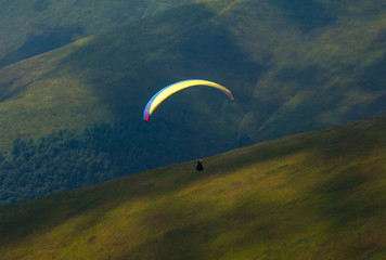 Paraglider flies over a mountain valley on a sunny summer day. Paragliding in the Carpathians in...