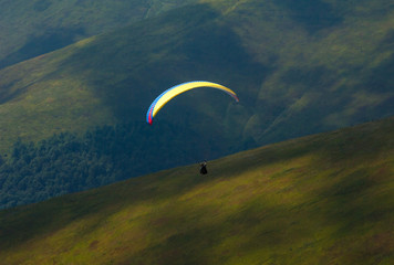 Paraglider flies over a mountain valley on a sunny summer day. Paragliding in the Carpathians in the summer.