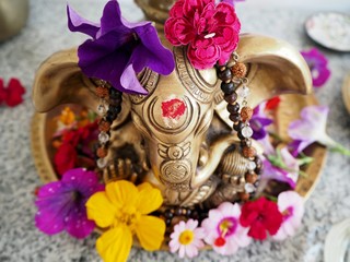 Hindu God Ganesha is covered with coloured flowers on an altar for a spiritual ceremony 